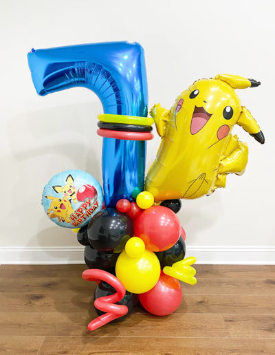 Blue number 7 balloon with a Pikachu balloon and a colorful balloon garland at the base, against a plain wall in Omaha.