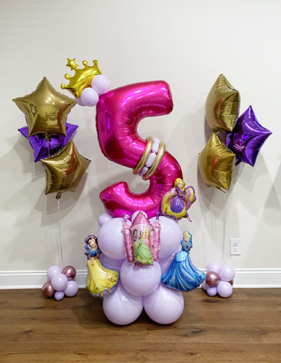A number 5-shaped pink balloon surrounded by gold and purple star balloons, with a balloon garland at the base featuring decorations inspired by Disney princesses.