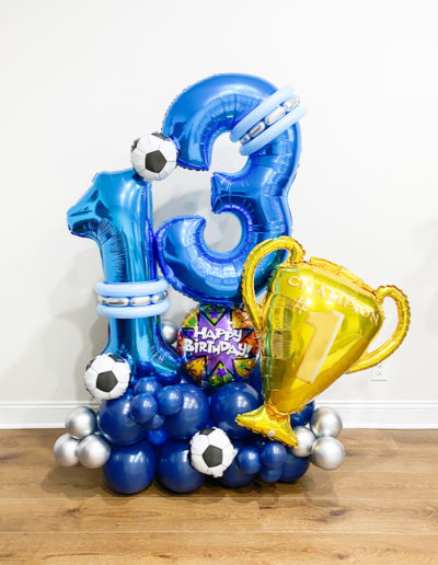 Blue and silver balloon arch featuring the numbers "3" and "7," soccer balls, and trophies, with "happy birthday" text in Omaha.