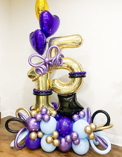 An elaborate balloon display in Omaha, Nebraska, featuring gold, purple, and blue balloons formed into shapes of numbers and accented with smaller balloons.