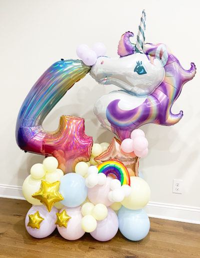 A colorful balloon arch, featuring a unicorn and stars, and dominated by a large number '4', arranged against a white wall.