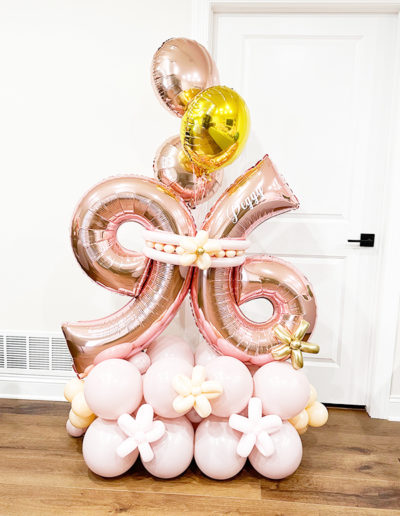A festive balloon arch featuring pink and gold balloons, with numbers "24" and the word "happy" for a birthday celebration in a room.