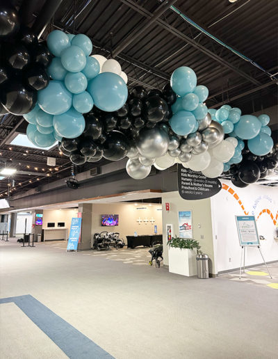 A large balloon garland in black and blue, designed by a skilled balloon decorator, adorns the Omaha corporate event space, complete with informational signage and seating areas.