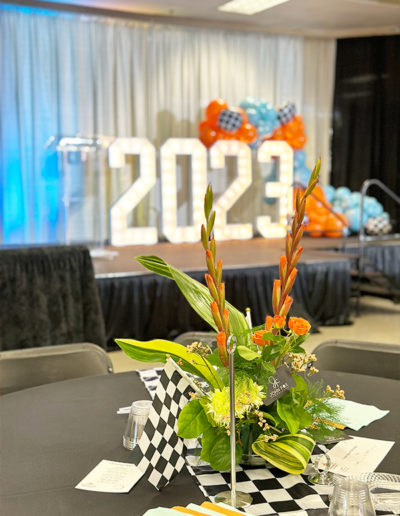 Decorated venue setup for a 2023 event in Nebraska featuring a large "2023" light-up sign, balloon garland, and a floral centerpiece on a table with a checkered tablecloth