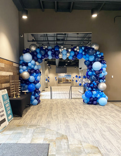 A hallway with a decorative arch made of blue balloons, crafted by a professional balloon decorator, leading to a room labeled "gathering 2023" at the end.