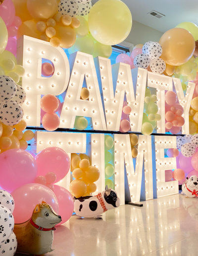 Large "pawty time" sign decorated with colorful balloons and dog-shaped balloon sculptures, enhanced by a balloon garland in a festive setting.