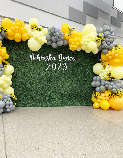 A decorative balloon arch with yellow and gray balloons over a green backdrop in Omaha that reads "Nebraska Dance 2023.