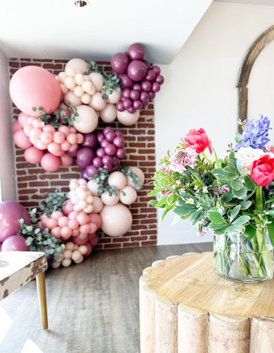 A stylish room corner in Omaha featuring a colorful balloon garland in shades of pink and purple, with a vase of vibrant flowers on a rustic wooden table.