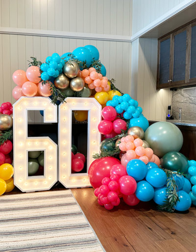 A large light-up number "60" in Omaha, decorated with a balloon arch featuring balloons in shades of blue, pink, and gold.