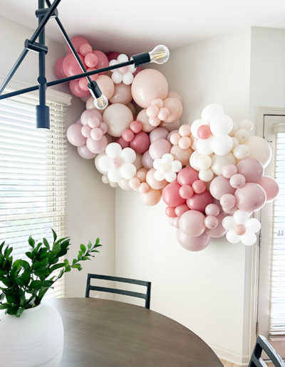 A heart-shaped balloon arch in pink and white hues hanging above a dining table in a well-lit room.