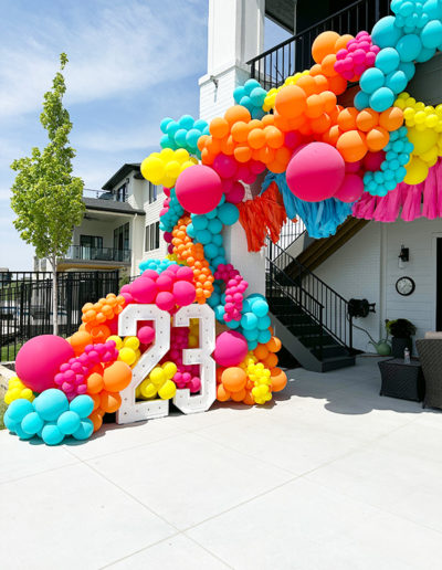 Colorful balloon garland installation on a staircase outside a home in Nebraska, celebrating a 21st birthday with large '21' figures surrounded by a cascade of vibrant balloons.